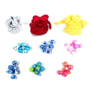 Può includere: Un set di sette sacchetti a cordoncino all'uncinetto in grigio, rosso e giallo, ognuno contenente un set di dadi colorati. I dadi sono di vari colori, tra cui blu, verde, rosa e bianco.