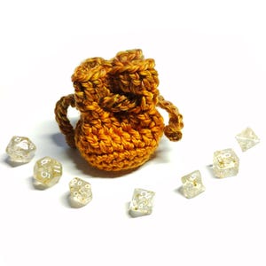 May include: A crocheted orange and brown pouch with a drawstring, sitting on a white surface with several clear dice with white numbers.