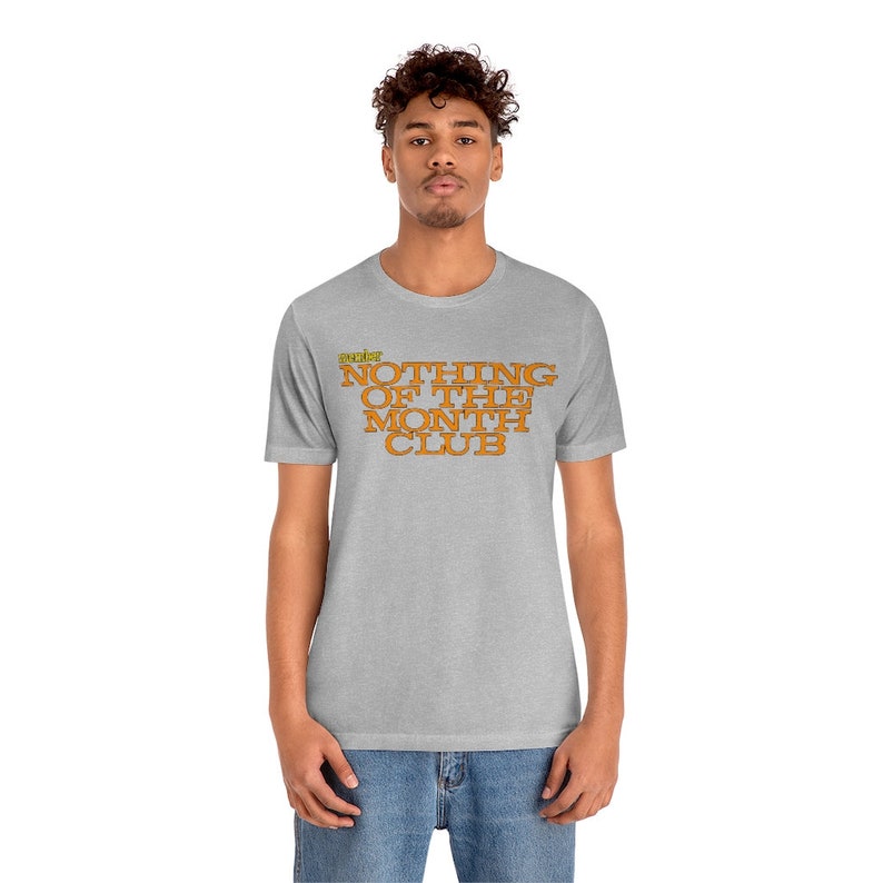 Peut inclure: Un t-shirt gris chin&eacute; avec le texte "The Nothing of the Month Club" imprim&eacute; en orange sur le devant.