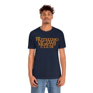 Peut inclure: Un t-shirt bleu marine avec le texte "member NOTHING OF THE MONTH CLUB" en lettres orange.