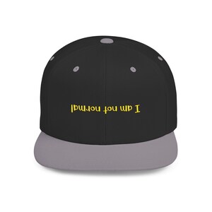 Pode incluir: Um boné de beisebol preto e cinza com o texto "I am not normal" bordado em amarelo na frente.