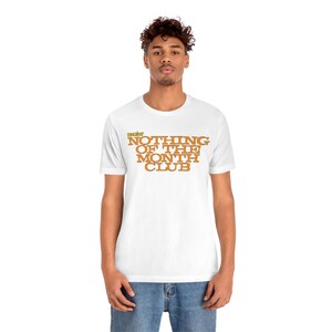 Peut inclure: T-shirt blanc avec le texte "The Best Nothing of the Month Club" en lettres orange et jaunes.