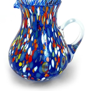 May include: A blue glass pitcher with a white, red, orange, and yellow speckled pattern. The pitcher has a clear glass handle.