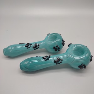 May include: Two turquoise glass smoking pipes with black paw print designs.