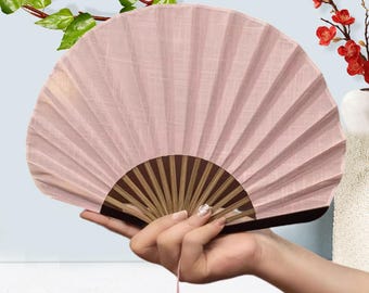 Può includere: Un ventaglio rosa con manico in legno. Il ventaglio è realizzato in tessuto plissettato e ha un nappa. Il ventaglio è tenuto in una mano.