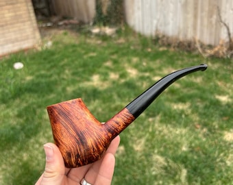 May include: A brown and black wooden smoking pipe with a curved stem. The pipe is held in a hand.