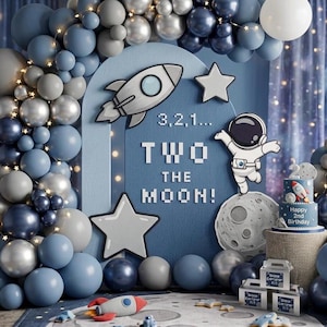 Puede incluir: Decoración de fiesta de cumpleaños con temática espacial con globos azules, plateados y blancos. Un telón de fondo presenta un cohete, estrellas y el texto "Two the Moon!". También hay una tarta con un cohete y "Happy 2nd Birthday".