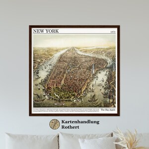 Op de afbeelding: Een vintage kaart van New York City uit 1873, die de indeling van de stad en de omliggende waterwegen laat zien. De kaart is ingelijst in bruin hout en bevat de tekst "NEW YORK" en "The Big Apple".