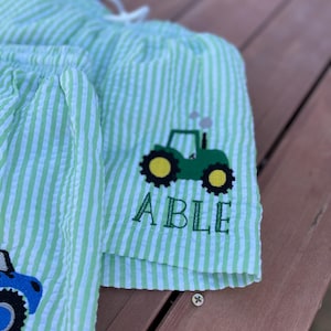 May include: Green and white striped shorts with a green tractor and the name "ABLE" embroidered on the front.