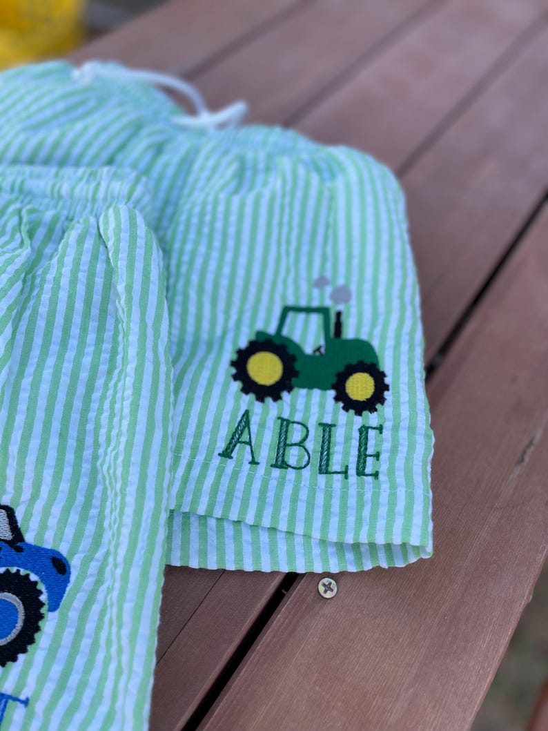 May include: Green and white striped shorts with a green tractor and the name "ABLE" embroidered on the front.