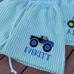 May include: Green and white striped shorts with a blue monster truck graphic and the name "EVERITT" embroidered on the front.