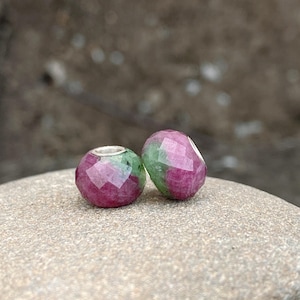 May include: Two green and pink gemstone beads with a faceted design. The beads are made of a natural stone and have a silver core.