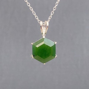 May include: A silver chain necklace with a green gemstone pendant. The pendant is a hexagonal shape with a faceted cut.