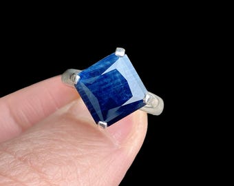 May include: A silver ring with a large, square-shaped blue sapphire gemstone.