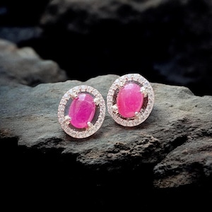 May include: A pair of silver earrings featuring pink oval gemstones set within a halo of smaller white gemstones.