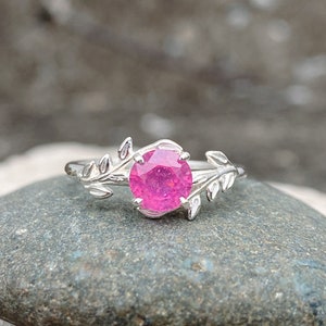May include: A silver ring with a pink gemstone set in a leafy design.