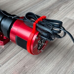 K&ouml;nnte beinhalten: Eine rote Astronomie-Kamera mit einem schwarzen Objektiv. Die Kamera hat einen schwarzen L&uuml;fter und mehrere schwarze Kabel mit den Aufschriften "ZWO" und "USB 3.0", die an sie angeschlossen sind.