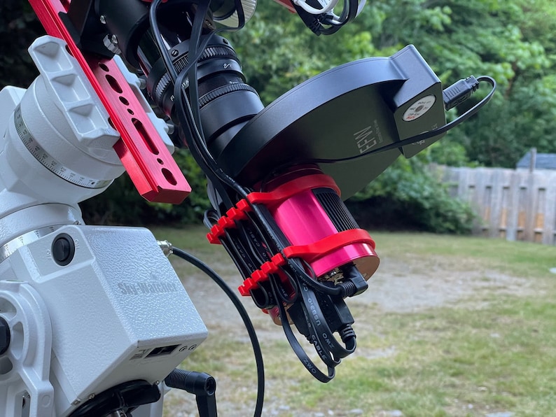 K&ouml;nnte beinhalten: Nahaufnahme eines Teleskops mit einer rot-wei&szlig;en Montierung, einer schwarzen Kamera und einem rosafarbenen Fokussierer. Das Teleskop ist mit einer schwarzen Box verbunden, auf der "EEV" steht. Das Teleskop ist auf einem wei&szlig;en Sockel mit der Aufschrift "Sky-Watcher" montiert.