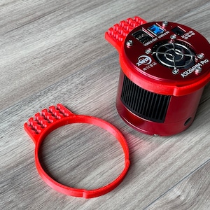 K&ouml;nnte beinhalten: Ein roter 3D-gedruckter Kamerahalter mit einem runden Ring und einer daran befestigten ZWO ASI294MM PRO Kamera. Die Kamera hat einen schwarzen L&uuml;fter und einen USB-Anschluss.