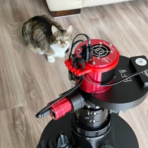 K&ouml;nnte beinhalten: Eine rote und schwarze Astronomie-Kamera mit einem K&uuml;hlventilator und einem schwarzen Netzteil. Die Kamera ist auf einer schwarzen Teleskopmontierung montiert.