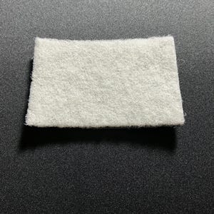 May include: A white, rectangular, felt-like fabric pad.