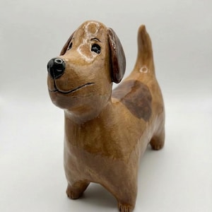 以下が含まれることがあります： 茶色の手作りのセラミック犬の置物。 犬は光沢のある仕上がりで、濃い茶色の耳と黒い鼻があります。 より濃い茶色の斑点が側面にあります。 犬は四本足で立っています。