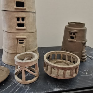 K&ouml;nnte beinhalten: Ein Satz unfertiger Leuchtturmst&uuml;cke aus Ton, bestehend aus dem Hauptturm, einem kleineren Turm, einem Gel&auml;nder, einem Sockel und einer Spitze. Die Teile befinden sich alle in verschiedenen Stadien der Fertigstellung, wobei einige detaillierter sind als andere.