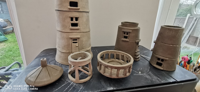 K&ouml;nnte beinhalten: Ein Satz unfertiger Leuchtturmst&uuml;cke aus Ton, bestehend aus dem Hauptturm, einem kleineren Turm, einem Gel&auml;nder, einem Sockel und einer Spitze. Die Teile befinden sich alle in verschiedenen Stadien der Fertigstellung, wobei einige detaillierter sind als andere.