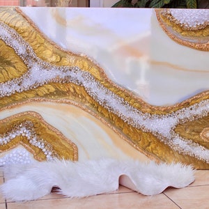 May include: Abstract art painting with white, gold, and beige colors. The painting features a flowing, organic design with a textured surface. The painting is framed and ready to hang.