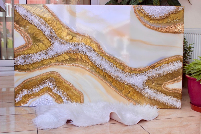 May include: Abstract art painting with white, gold, and beige colors. The painting features a flowing, organic design with a textured surface. The painting is framed and ready to hang.
