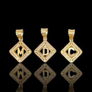 May include: Three gold pendants with diamond-like accents, each featuring a different letter: M, D, and C. The pendants are displayed against a black background.