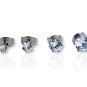 May include: Four pairs of silver stud earrings with clear round cubic zirconia stones. The earrings are arranged in a row from smallest to largest.