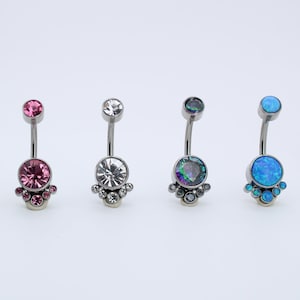May include: A set of six belly button rings with different colored gemstones. The rings are made of surgical steel and have a curved barbell design. The gemstones are set in a cluster of smaller stones.