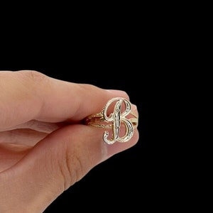 Puede incluir: Un anillo de oro con un diseño de letra B en cursiva.