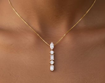 May include: A gold necklace with a pendant featuring a marquise-cut diamond, a round diamond, a baguette-cut diamond, another round diamond, and an oval-cut diamond. The chain is a delicate gold box chain.