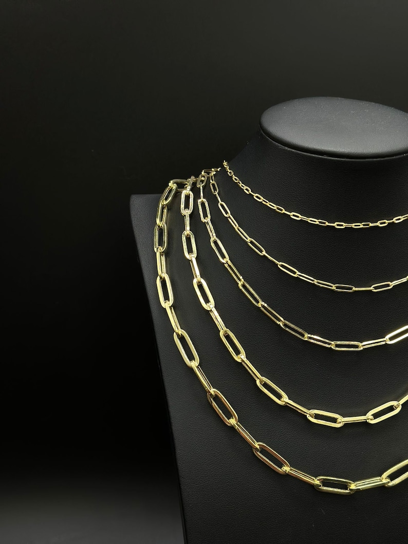 May include: A set of six gold chain necklaces of varying lengths, displayed on a black velvet stand. The chains are made of oval-shaped links.