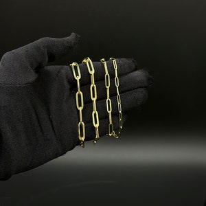 May include: Four gold chain necklaces with a link style that resembles a paperclip. The chains are arranged in a stack, with the largest chain at the bottom and the smallest chain at the top.