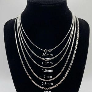 May include: A display of several silver box chain necklaces of varying thicknesses, ranging from .80mm to 3mm, against a black background. Each chain is shown with its corresponding size measurement in millimeters.