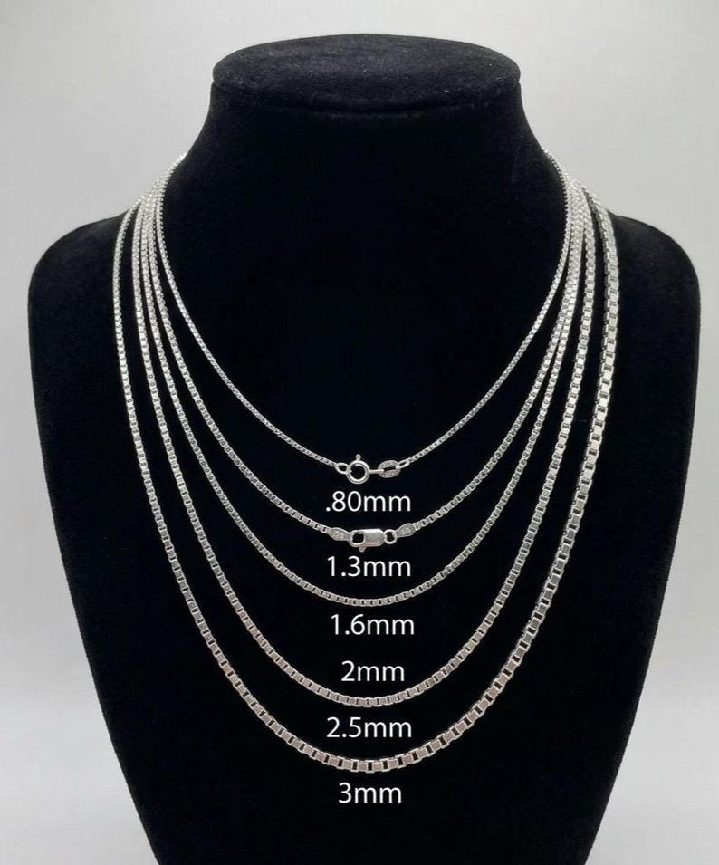 May include: A display of several silver box chain necklaces of varying thicknesses, ranging from .80mm to 3mm, against a black background. Each chain is shown with its corresponding size measurement in millimeters.