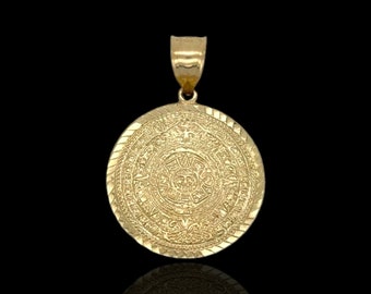May include: A gold pendant featuring a detailed depiction of the Aztec calendar, known as the Sun Stone. The pendant is round and has a textured surface.