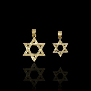 Op de afbeelding: Twee gouden Davidster-hangers, een groter dan de andere, op een zwarte achtergrond.