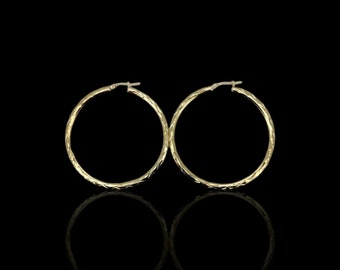 May include: A pair of gold hoop earrings with a textured surface. The earrings are round and have a polished finish.