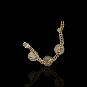 May include: A gold chain bracelet with a mariner link design. The bracelet is adorned with small, clear stones and features three silver coins attached to the links.