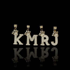 May include: Five gold pendants with a crown on top and a letter in the center. The letters are K, M, R, and J. The pendants are set with clear stones.