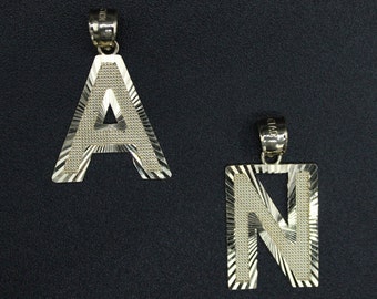 May include: Two gold-tone pendants, one shaped like the letter A and the other shaped like the letter N. Both pendants have a textured, diamond-like pattern.