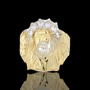 May include: A gold-tone pendant featuring a detailed depiction of Jesus Christ's face with a crown of thorns. The pendant is made of metal and has a textured surface.