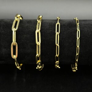 May include: Four gold chain bracelets of different lengths and widths, displayed on a black velvet background.
