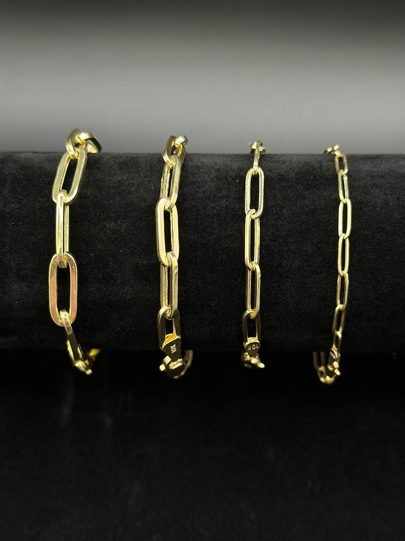 May include: Four gold chain bracelets of different lengths and widths, displayed on a black velvet background.