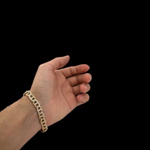 May include: A gold chain bracelet with a mariner link design. The bracelet is on a person's wrist.