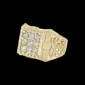 May include: A gold ring with a square-shaped center set with clear stones and a filigree design on the band.